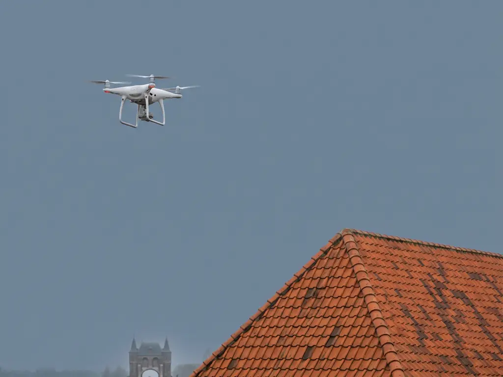 Witte professionele drone zweeft boven traditioneel Nederlands dak met terracotta pannen, Waterpoort van Sneek zichtbaar op achtergrond