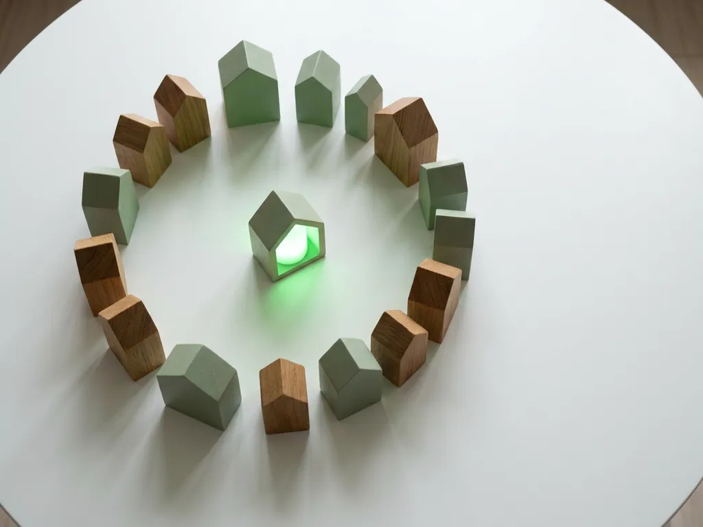 Cirkel van houten huissilhouetten op wit oppervlak, één huis oplichtend met zacht groen licht als symbool voor duurzame energie.
