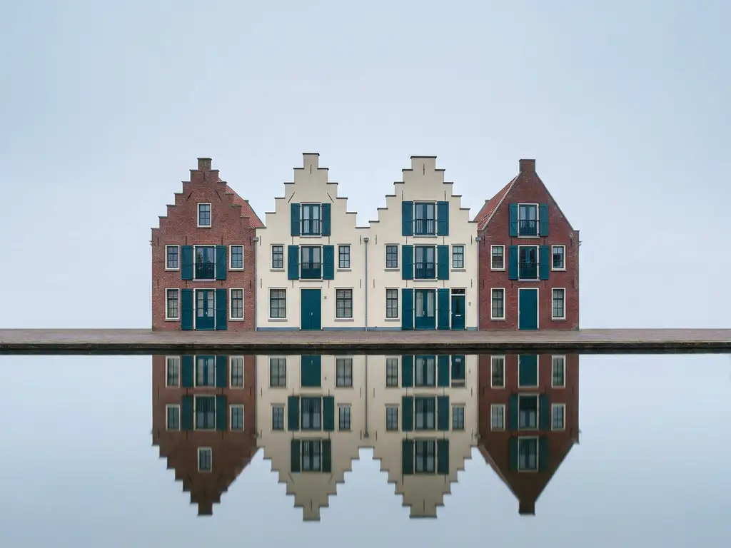 Traditionele Friese grachtenpanden met trapgevels weerspiegeld in kalm water onder een bewolkte hemel