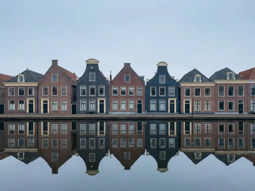 Friese grachtenpanden met trapgevels weerspiegeld in kalm water, gedempte baksteenrode en leisteenblauwe tinten onder diffuus noordelijk licht.