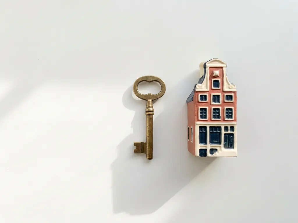 Koperen sleutel naast miniatuur Fries grachtenpand op witte ondergrond, zacht ochtendlicht met subtiele schaduwen.