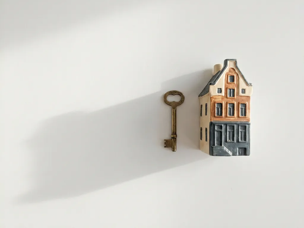 Koperen sleutel naast miniatuur grachtenpand met trapgevel op witte ondergrond in zacht ochtendlicht